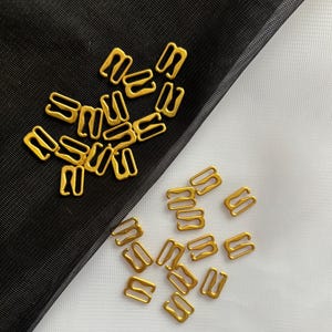 May include: A pile of gold-colored metal bra strap adjusters on a black and white background.