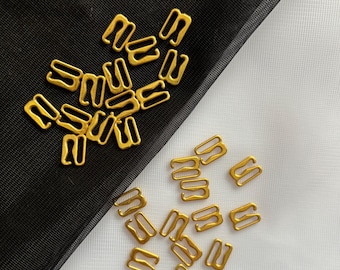 May include: A pile of gold-coloured metal bra strap adjusters on a black and white background.