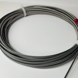 May include: A coil of silver-colored, braided wire with a textured surface. The wire is coiled in a circle and is tied with a white zip tie.