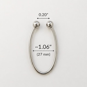 Könnte beinhalten: Ein silberfarbenes, oval geformtes Metallobjekt mit zwei kleinen, runden Kugeln oben. Das Objekt ist etwa 2,7 cm lang und 0,5 cm breit. Das Design ist schlicht und modern, mit poliertem Finish.