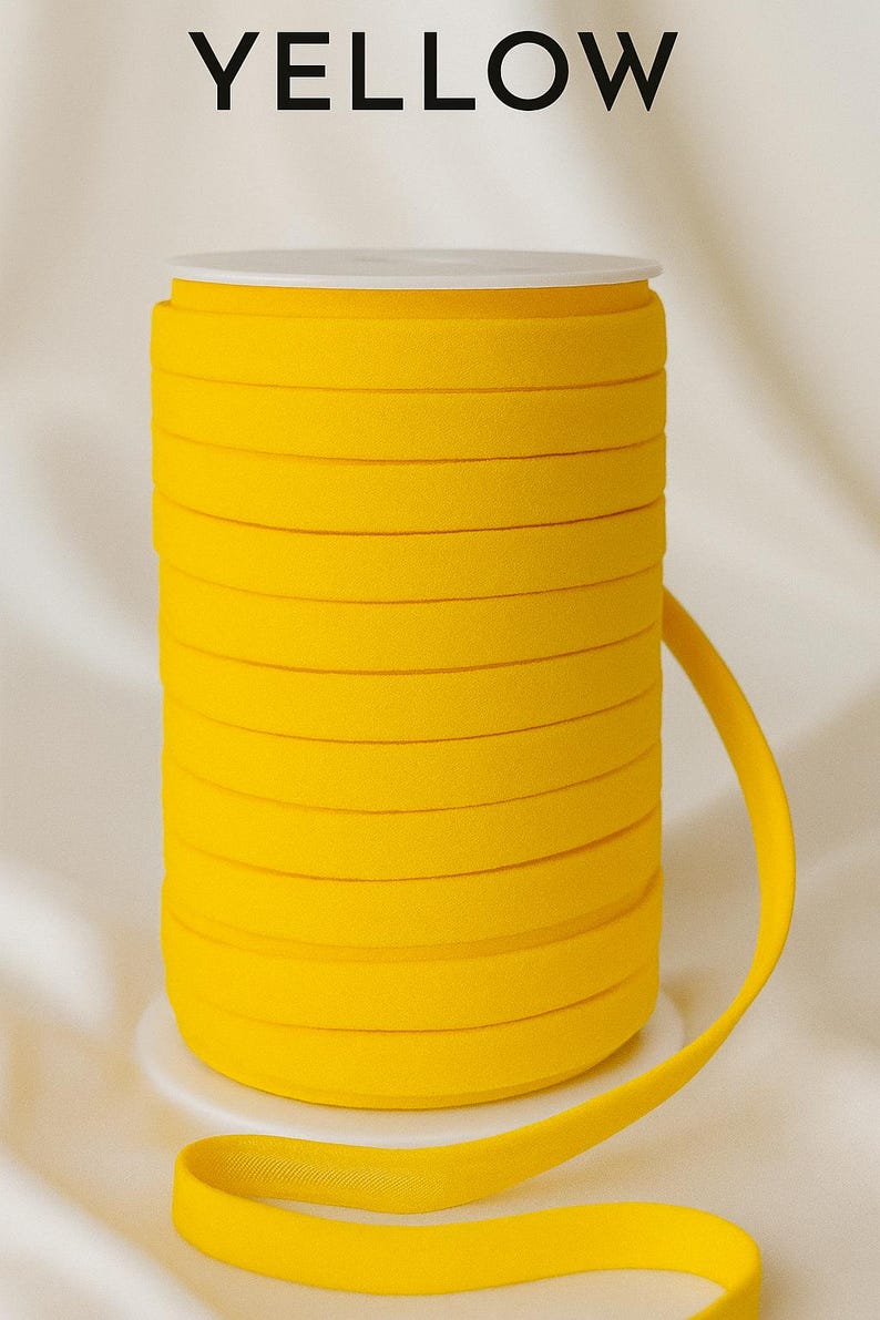 May include: A spool of bright yellow elastic ribbon. The ribbon is tightly wound and sits on a white base. The word "YELLOW" is printed in black at the top of the image. The ribbon is unwound slightly, showing its flexibility.