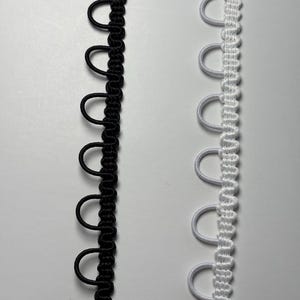 以下が含まれることがあります： 2本の装飾トリムのクローズアップ。1本はループ状のディテールが施された黒色、もう1本は同様のループ状のディテールが施された白色です。トリムは、縫製やクラフトプロジェクトに使用される可能性があります。