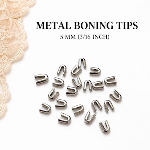 May include: A collection of small, U-shaped silver-coloured metal boning tips scattered on a white surface. The text METAL BONING TIPS 5 MM (3/16 INCH) is printed in black above the metal pieces, which are used for finishing corset boning.