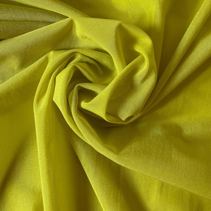 May include: Close-up of a vibrant, chartreuse-colored fabric. The material is finely woven, with a slight sheen, and is gathered in soft folds, creating a textured, swirling pattern. The fabric appears lightweight and possibly suitable for apparel or decorative projects.