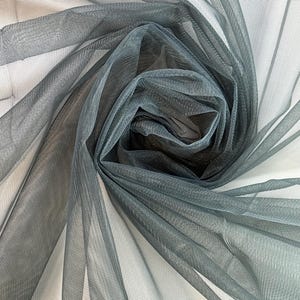 Puede incluir: Primer plano de una tela transparente de color gris oscuro con una textura de malla fina. La tela está drapeada y doblada, creando un efecto suave y fluido.