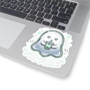 May include: A sticker featuring a cartoon ghost holding a boba tea. The ghost is white with a silver outline and has a friendly expression. The text "I'M FINE" is written below the ghost in a playful font. The sticker is on a laptop.