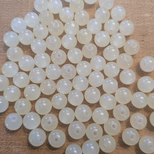 May include: A pile of white, round, smooth beads. The beads are made of a translucent material and have a slight iridescent sheen.