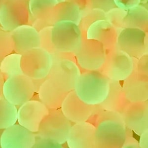May include: A close-up of a group of small, round, translucent orbs in shades of green and yellow. The orbs are arranged in a random pattern, creating a visually appealing and textured surface.