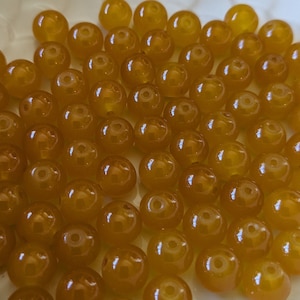 May include: A large group of round, amber-colored beads. The beads are smooth and shiny, and they are all about the same size.