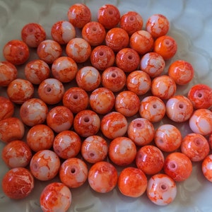 May include: A collection of orange and white marbled glass beads. The beads are round and have a speckled appearance.