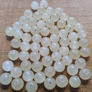 May include: A pile of white iridescent round beads. The beads are smooth and have a slight shine to them.