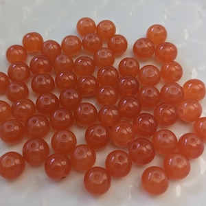 May include: A collection of approximately 50 round, orange beads. The beads are made of a smooth, translucent material and have a slight shine.