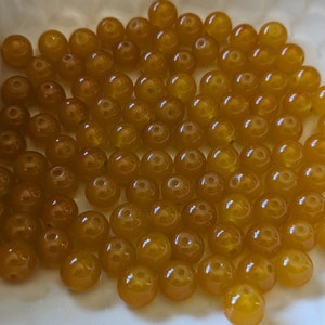 May include: A close-up of a pile of round, yellow beads. The beads are smooth and shiny, and they are all about the same size.