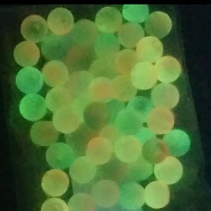 May include: A close-up of a group of green and orange glow-in-the-dark marbles.