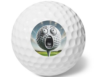 May include: A white golf ball with a cartoon face on it. The face is wide-eyed and has its mouth open in a surprised expression. The golf ball is on a tee and the background is a green golf course.