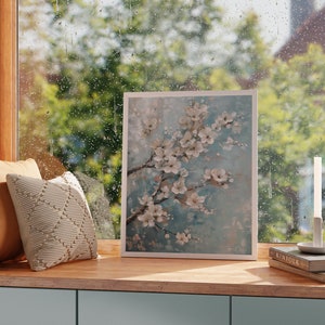 K&ouml;nnte beinhalten: Ein gerahmtes Gem&auml;lde mit einer wei&szlig;en Blumenanordnung auf blauem Hintergrund. Das Gem&auml;lde h&auml;ngt an einer Wand &uuml;ber einem Holzregal mit einem Buch und einer Kerze.