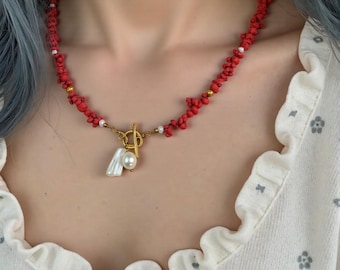 May include: A red beaded necklace with a gold toggle clasp and a pearl and shell pendant.