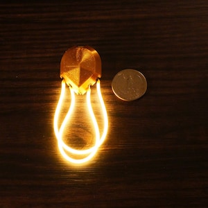 May include: A gold-coloured, geometric-shaped light with a white LED light source. The light is attached to a thin, white, flexible cord.