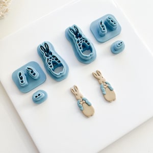 May include: A set of blue plastic cookie cutters shaped like a rabbit, along with two smaller cutters for the rabbit's ears and nose. Two brown fondant rabbits are also shown.
