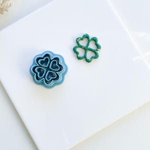 May include: A set of three blue plastic cookie cutters shaped like four-leaf clovers. The cutters are stacked on top of each other. A green four-leaf clover cookie cutter is shown next to the set.