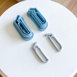 May include: Four blue plastic cookie cutters shaped like the numbers 1 and 0, and two small blue plastic cookie cutters shaped like a hook.