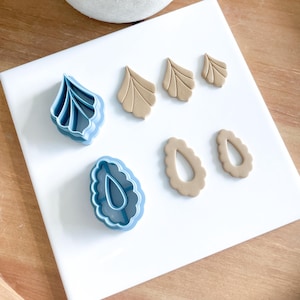 May include: A set of blue polymer clay cutters for crafting earrings. The cutters are shaped like leaves and teardrop shapes. There are also three brown clay earrings that have been cut out using the cutters.