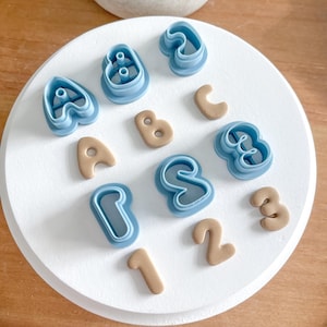 May include: A set of blue plastic cookie cutters shaped like the letters A, B, C, S, and the numbers 1, 2, 3. There are also brown fondant letters and numbers.