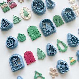 May include: Assortment of Christmas-themed cookie cutters in various shapes, including trees, gingerbread men, and ornaments. The cutters are blue, and the cookies are decorated with green, red, and white icing. Perfect for holiday baking.