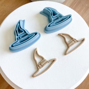 May include: Four witch hat cookie cutters, two are blue and two are brown. The blue cutters are detailed with a buckle and brim. The brown cutters are simple outlines.