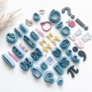 May include: A set of 30 blue plastic cookie cutters in various shapes, including an apple, a bow, a pig, a paintbrush, a tube of glue, a paint palette, a question mark, an exclamation point, and a number pi.