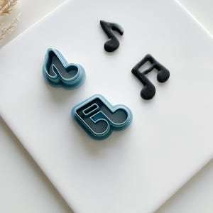 May include: Three music note cookie cutters, two are blue and one is black. The blue cutters are made of plastic and the black cutter is made of fondant.
