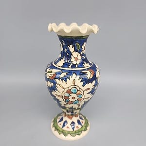 Może przedstawiać: Ceramiczny wazon z falbanką, z niebiesko-białym wzorem kwiatowym. Wazon ma podstawę na cokole z zielono-białym wzorem. Całość utrzymana w tradycyjnym, dekoracyjnym stylu.