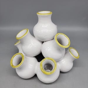 May include: A white ceramic tulip vase with a cluster of openings, each outlined in yellow. The vase has a glossy finish and a unique, sculptural design. This decorative vase is ideal for displaying flowers.