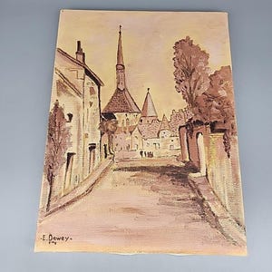 Puede incluir: Pintura al óleo de un pueblo europeo, con una carretera que conduce a una iglesia con una alta aguja. La obra de arte utiliza tonos marrones y beige. La firma del artista, "E. Dewey", es visible en la esquina inferior izquierda.