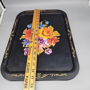 May include: Black rectangular serving tray with a floral design. The tray features a bouquet of colorful flowers in the center and gold trim along the edges. A wooden ruler is placed on top of the tray, measuring approximately 18 inches.