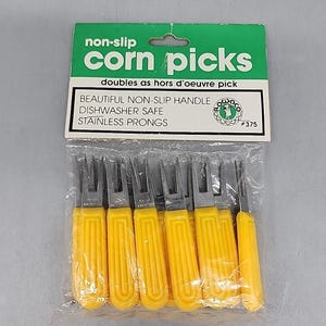 May include: Package of corn picks with yellow handles and stainless steel prongs. The packaging reads "non-slip corn picks" and "doubles as hors d'oeuvre pick". The package also states "dishwasher safe".