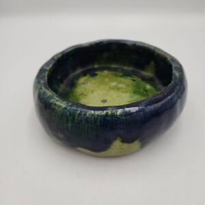 Può includere: Una piccola ciotola in ceramica fatta a mano, di forma rotonda con una finitura lucida. L'interno presenta una miscela screziata di smalto verde lime e blu scuro, mentre l'esterno è prevalentemente blu scuro con macchie di verde lime.