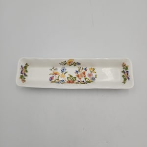 May include: A rectangular white ceramic tray with scalloped edges, featuring a colorful floral pattern with blue, yellow, pink, and green flowers, along with a central butterfly motif and additional butterfly accents on the far left and right sides.