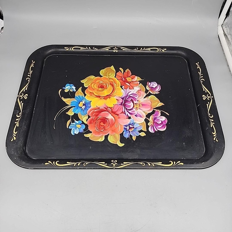 May include: Black rectangular serving tray with rounded corners. The tray features a colorful floral bouquet in the center, with gold decorative accents along the edges. The flowers include orange, yellow, purple, and blue blooms.