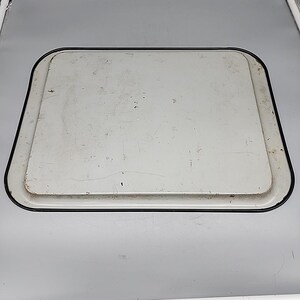 May include: A rectangular, off-white metal tray with a black border. The tray has a slightly raised edge and a worn appearance, suggesting it is vintage or has been well-used. The surface shows minor imperfections.