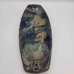 Könnte beinhalten: Eine ovale dekorative Schale mit einem marmorierten Design in Blau-, Grün- und Pfirsichtönen. Die Schale hat eine glänzende Oberfläche und an jedem Ende ein silbernes Rosendesign. Die Schale ist etwa 25 cm lang.