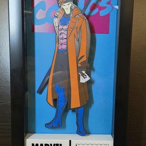 May include: A framed illustration of a comic book character, Gambit, from Marvel Comics. The illustration is in a 3D style, with Gambit standing in front of a blue background. The frame includes a white label with the text "MARVEL COMICS GROUP $1.00 #97" and a stamp with the text "APPROVED BY THE COMICS CODE AUTHORITY".