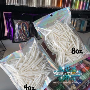May include: Two clear plastic bags filled with white, thin, and long beads. The bag on the left has a label that says "4oz" and the bag on the right has a label that says "8oz". The bags are labelled with "Chrissy's Creations Indigenous Beadwork & Supplies".