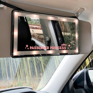 以下が含まれることがあります： LEDライト内蔵の黒い車のサンバイザーミラー。ミラーは白い縁取りがあり、ミラーには「PASSENGER PRINCESS」の文字が印刷されています。