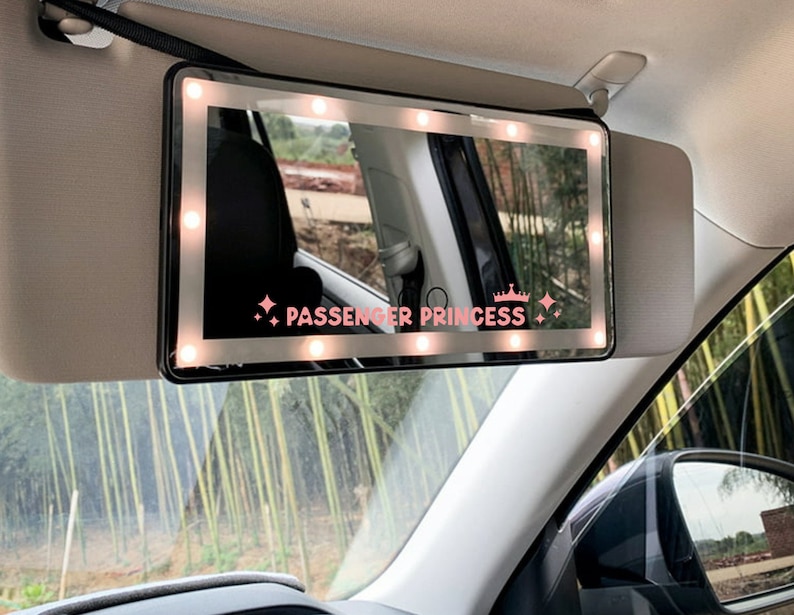 以下が含まれることがあります： LEDライト内蔵の黒い車のサンバイザーミラー。ミラーは白い縁取りがあり、ミラーには「PASSENGER PRINCESS」の文字が印刷されています。