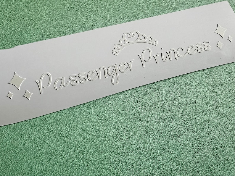 以下が含まれることがあります： 「Passenger Princess」というテキストが筆記体で書かれた白いステッカー。テキストの上と下に王冠と2つのダイヤモンドの形があります。