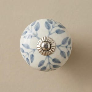 以下が含まれることがあります： 白いセラミック製のキャビネットノブ、青い葉の模様。ノブは銀色の金属ベースです。この装飾的なハードウェアは、あらゆる家具にエレガンスを添えるのに最適です。