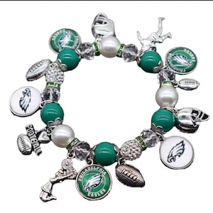 May include: A stretch bracelet featuring green and white beads, clear faceted beads, and silver-toned charms. The charms include Philadelphia Eagles logos, footballs, helmets, a cheerleader, and a charm with the word FOOTBALL engraved on it.
