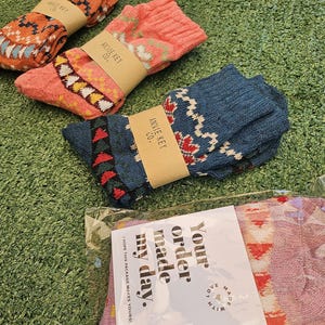 May include: Three pairs of colorful patterned socks with the brand name "Annie Key Co." on the packaging. The socks are packaged in a clear plastic bag with a white tag that says "Your order made my day."