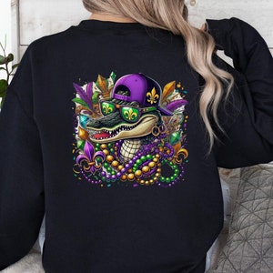 May include: Black sweatshirt with a purple and green alligator wearing a purple and gold Mardi Gras hat and sunglasses. The alligator is surrounded by Mardi Gras beads and other decorations.